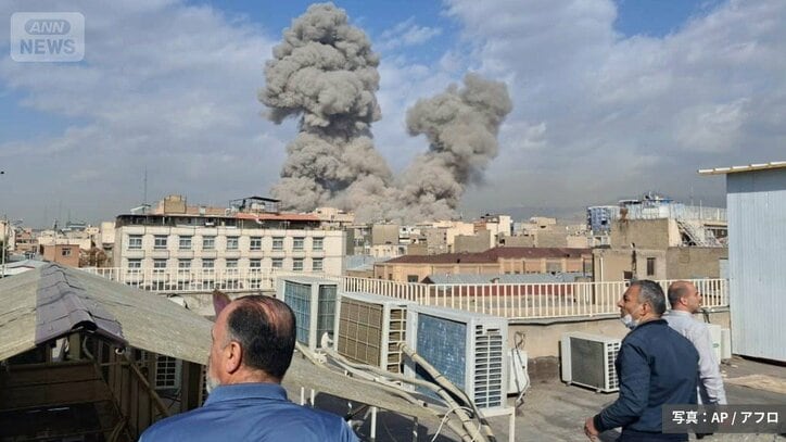 イランの首都テヘランで爆発が起こり、空に立ち上る煙を見守る人々（写真：AP/アフロ）